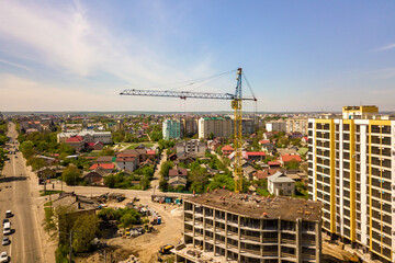 Apartment or office tall building under construction. Working builders and tower cranes on bright...