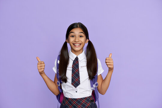 Excited Indian Kid Primary School Girl With Backpack Wearing Uniform Showing Thumbs Up Isolated On Violet Background. Happy Latin Child Student Celebrating Freedom, Recommending Best Education Choice.