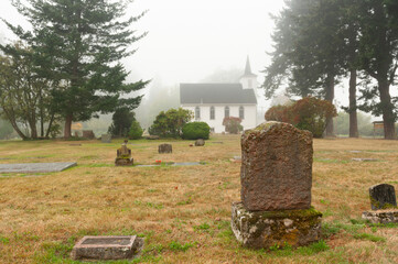 Headstone in a Small Cemetery Behind a White Wooden Church. Historic cemetery dating back to the...