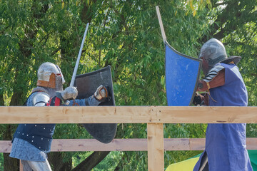 Two knights on foot in heavy medieval armor fight with swords. They are protected by iron helmets...