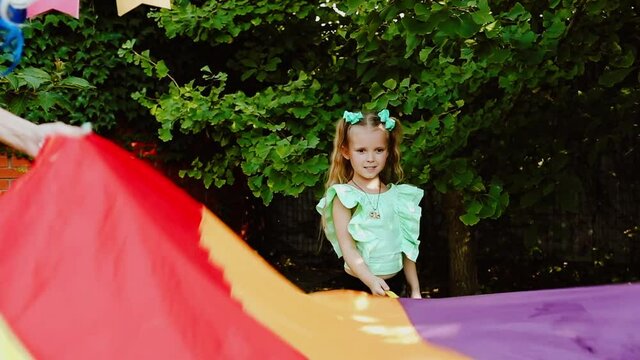 Children playing with colourful toy parachute in the garden. Slow motion video.
