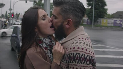 Middle-aged man and woman in love kissing on the street of a busy city in autumn in cloudy weather. A man in a sweater kissing a woman in a coat. - Powered by Adobe