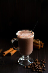 cup of cacao. glass of hot chocolate with whipped cream, coffee beans and cinnamon sticks on a dark background. hot drinks on a wooden background. winter and autumn. vertical. copy space