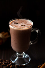 cup of cappuccino with chocolate. hot chocolate with whipped cream, marshmallows, coffee beans and cinnamon sticks on a dark background. hot drinks on a wooden background. winter and autumn. vertical
