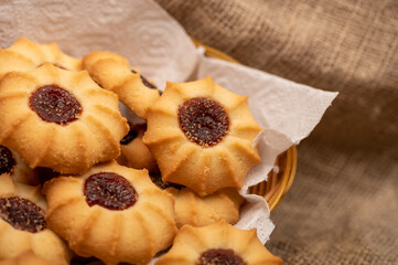 Homemade pastry cookies with jam in a wicker basket on a background of homespun fabric with a rough texture, close-up, selective focus.