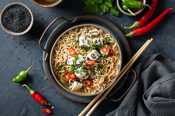Asian food, ramen with tofu and vegetables in ceramic bowl on dark background, top view