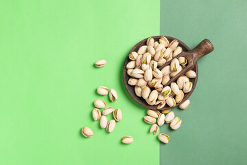 Flat lay composition of pistachios on wooden spoon and dish on green background . with  copy space.