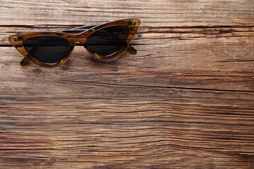Stylish sunglasses on wooden background, top view. Space for text