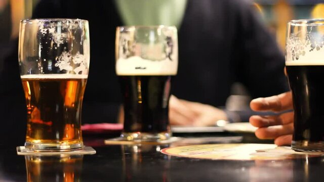 Beer pints of friends on background drinking in a pub at night, closeup mugs of draft root and light beer on the table, dark scene