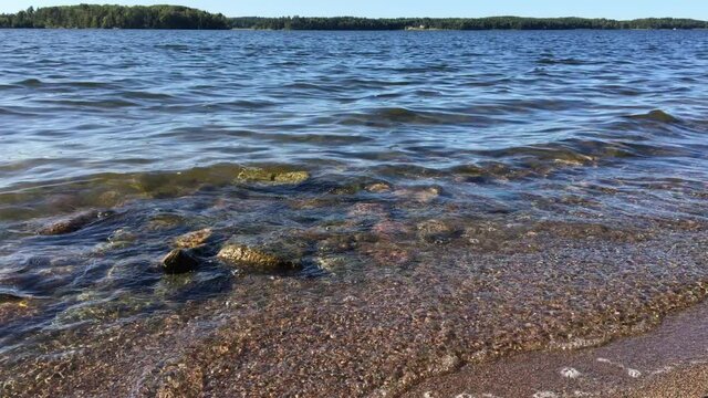 Small waves touching the beach shore a sunny day at a Swedish lake called Malaren or Malar. Clear fresh water, very transparent. Nice weather and climate. G&ouml;rv&auml;ln, J&auml;rf&auml;lla, Stockholm, Sweden.