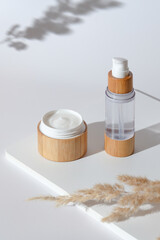 Natural organic cosmetics set with dried flowers on white podium. Face cream jar and lotion in eco friendly bamboo packaging. Zero waste