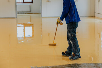 Worker, coating floor with self-leveling epoxy resin in industrial workshop.