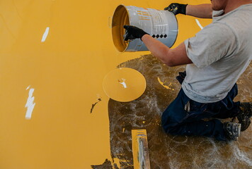 Worker, coating floor with self-leveling epoxy resin in industrial workshop.