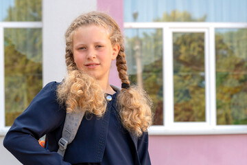 Portrait of a schoolgirl on the background of the school. Concept  school days, Back to school. girl in a  uniform with a backpack. pupil, learner, scholar.