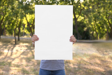 Woman holding blank poster outdoors. Mockup for design