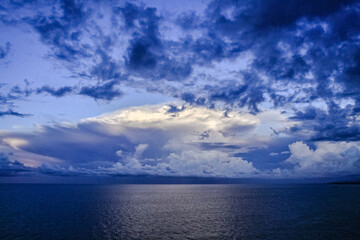 Obraz premium Panoramic view of ocean waters horizon line with dramatic cumulus thunderstorm cloudscape in blue sky background.