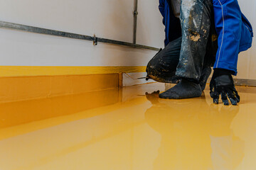 Worker, coating floor with self-leveling epoxy resin in industrial workshop.
