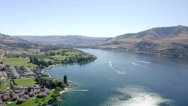Drone flying over houses towards lake and mountains. 4k Lake Chelan aerial footage. Scenic mountains around lake. Beautiful lake drone footage.