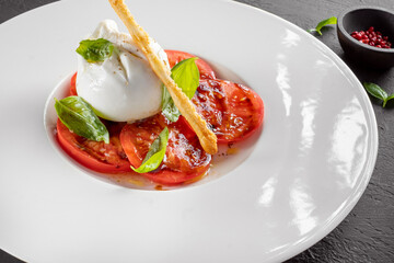 Burrata cheese and tomato salad with Basil and olive oil served on a white plate