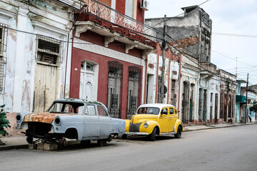 small yellow car and broken blue car parked on the street in cuba