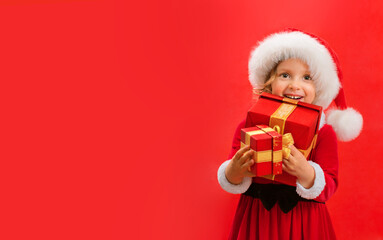 Smiling funny child in Santa red hat holding Christmas gift in hand.