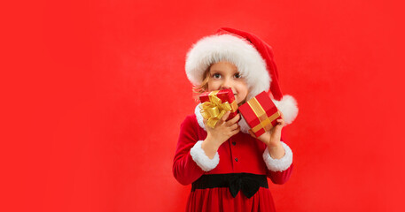 Funny child in Santa red hat holding Christmas gift in hand.