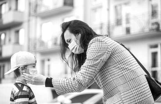 Mother puts a safety mask on her son's face. Schoolboy is ready go to school. Cute boy with a backpack outdoors. Black and white