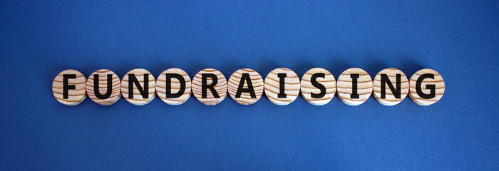The word 'fundraising' on wooden circles on blue table. Beautiful background, copy space. Business...