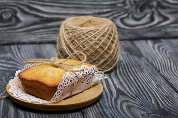 Freshly baked cupcake on a napkin. Tied with twine. Nearby is a reel of rope. Against the background of black pine boards.