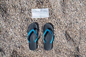 Covid-19 reality: facial protective mask required to enter the beach. Mask and flip-flops on pebble