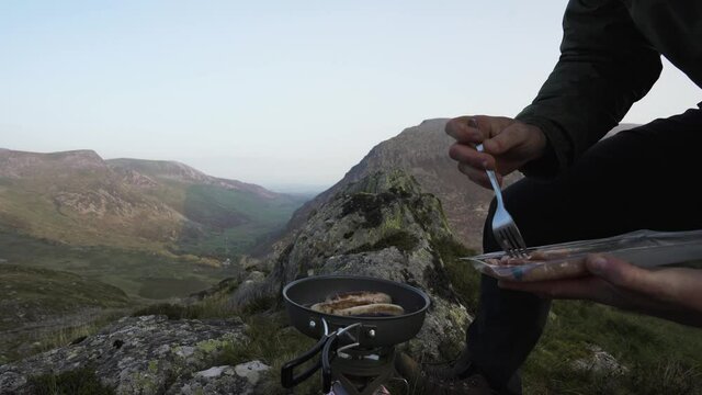 Man cooking bacon in a frying pan while camping in the mountains
