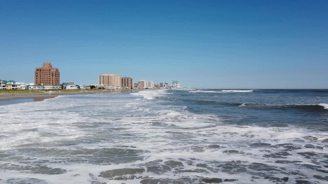 View along an Atlantic Ocean coastline with waves breaking as they approach the shore. Atlantic City is seen in the distance.