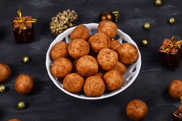 Traditional German Christmas sweets called 'Marzipankartoffeln'. Round ball shaped almond paste pieces covered in cinnamon and cocoa powder in white bowl on dark background