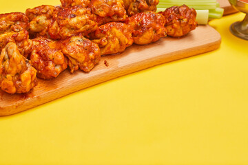 Buffalo chicken wings on a wooden board with celery on a yellow background, copy space