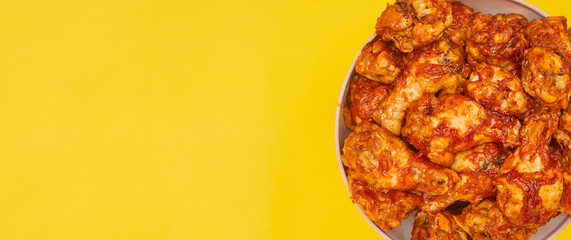 Buffalo chicken wings in a bowl on a yellow background, copy space