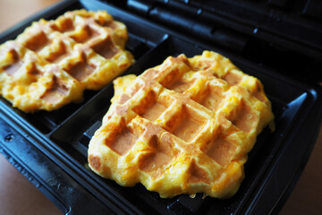 side view of two fresh Belgian waffles made from cornmeal eggs and pumpkin lie in a waffle iron while cooking.  home cooked gluten free food