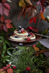 Japanese pancakes with berries in a white plate on green moss stands against a background of bright autumn leaves.