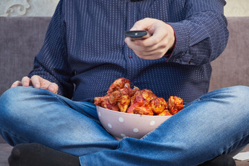 man watching tv on the couch with a plate of Buffalo Chicken Wings, copy space