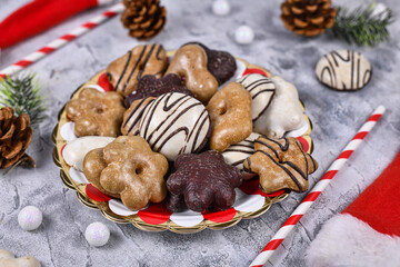 Obraz na płótnie Canvas Traditional gingerbread cookies with sugar and brown and white chocolate glazing on striped plate surrounded by seasonal Christmas decoraion