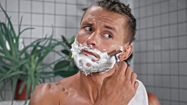 Man with towel shaving with safety razor in bathroom