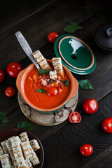 Tomato puree soup with croutons and herbs in a small ceramic saucepan on a dark wooden table. Vegetarian seasonal food.