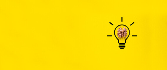 on a yellow background there is a half of a walnut. concept idea in the human brain - a light bulb is on