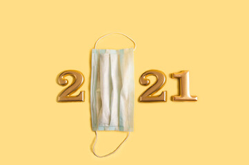 Happy New Year 2021. Numbers 2021 in gold and a medical mask on a yellow background. Covid 2019 and New Year lettering numbers.