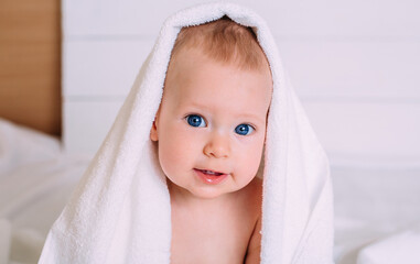 A cute baby with blue eyes wrapped in a towel as the hood looks into the camera.