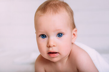 A cute baby with blue eyes wrapped in a white towel looks at the camera.