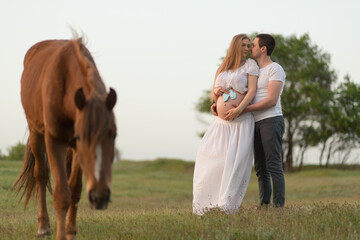 A farmer with his pregnant wife at sunset on his farm. Posing with a horse