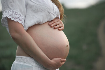 Pregnant blonde girl in white in a green field. Rural natural landscape