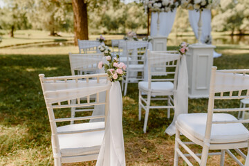 Wedding ceremony outdoors in the park. White chairs decorated with roses.