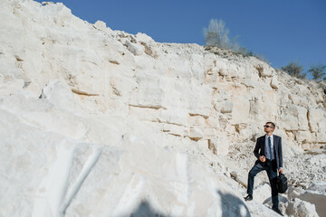 Young man businessman with a briefcase and jacket is climbing the mountain.