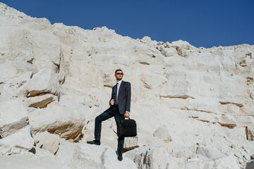 Young man businessman with a briefcase and jacket is climbing the mountain.